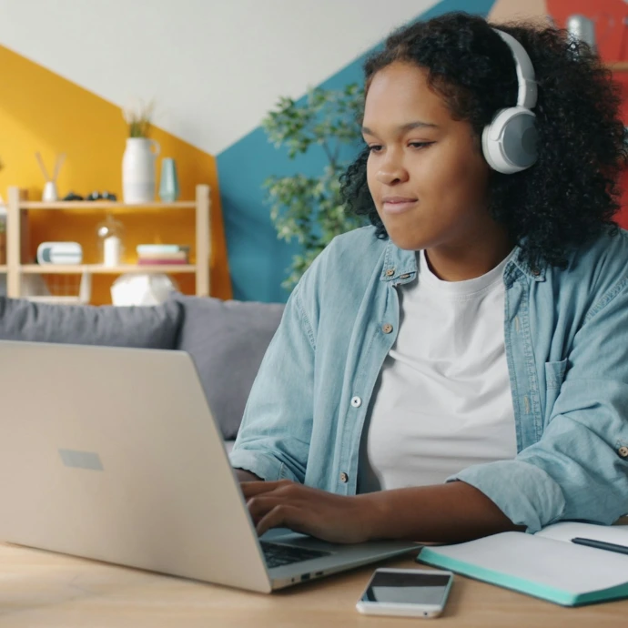 Young woman wearing headphones using laptop at desk.